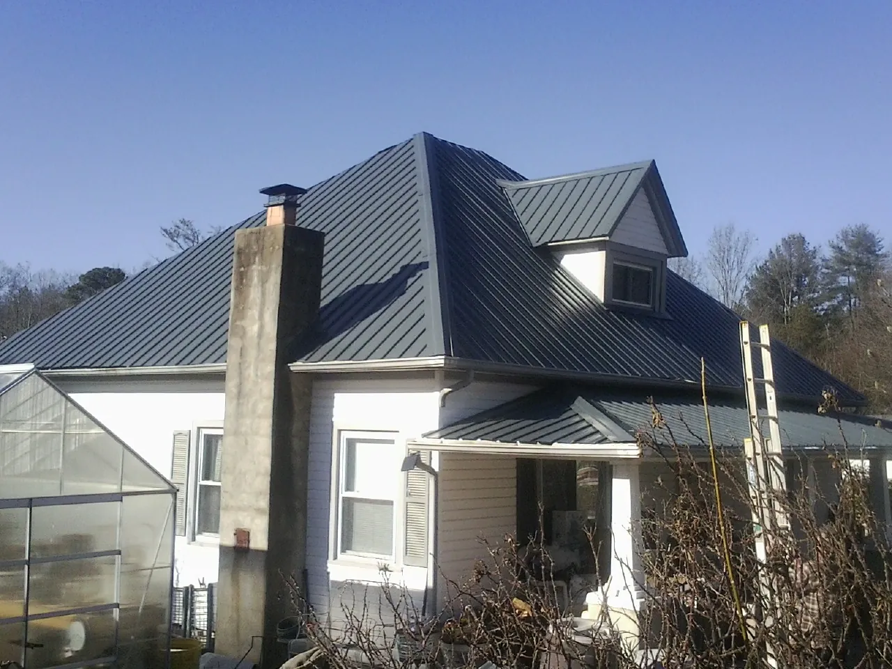 Dark blue standing seam metal roof on a white farmhouse with dormer — Slate & Tile Roof Repair by Roofing Brothers in Boswell