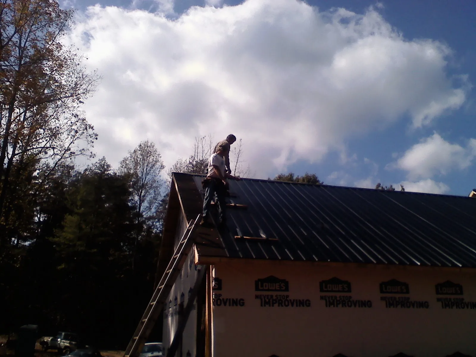 Roofer fastening dark metal panels high against a cloudy sky, from a Roof Inspection job in Boswell