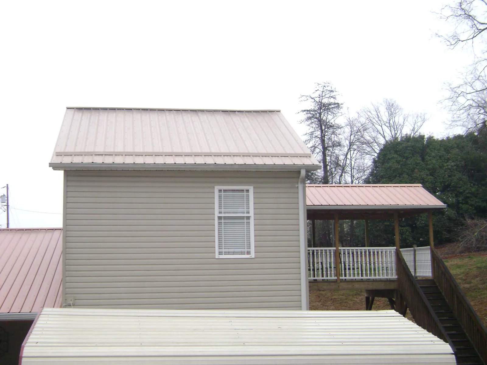 Tan metal roofs on a two story addition and attached porch, from a Roof Replacement job in Boswell